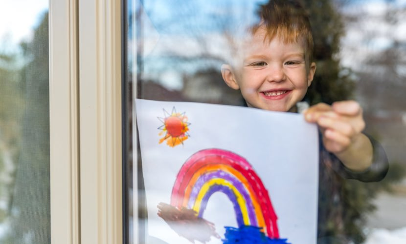 Boy sticking drawing of rainbow on window